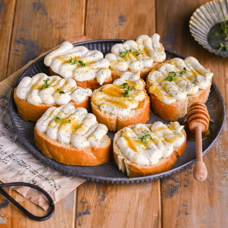 galvanized plate with 7 pieces of crositin topped with whipped ricotta and honey