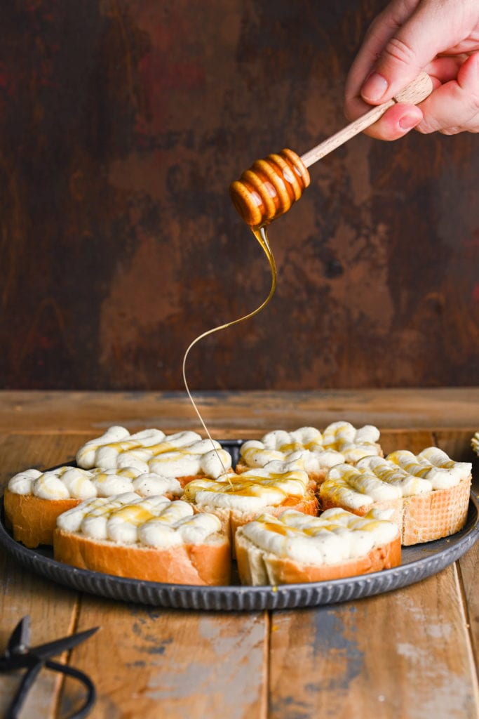 using a honey dipper to driizzle honey over whipped ricotta crostini