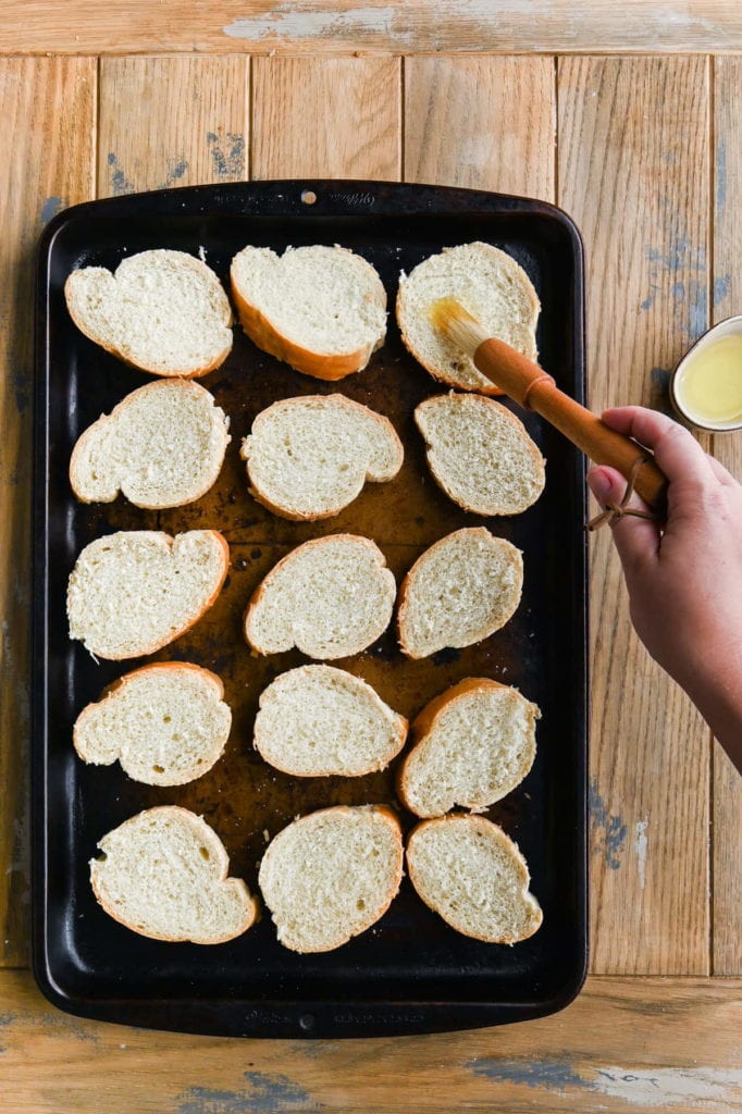 using a pastry brush to brush olive oil on sliced french baguette