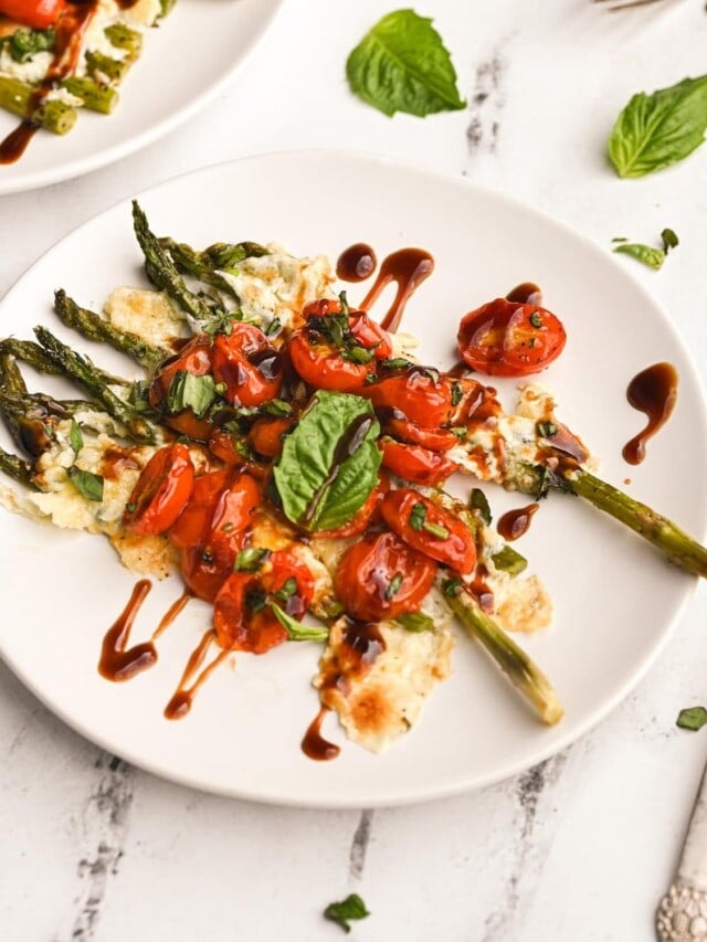 plate of asparagus with melted cheese, roasted tomatoes, basil, and balsamic glaze