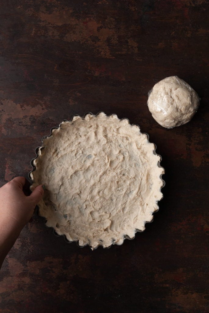 splitting pie crust dough in half and using clean hands to push one half into a pie dish