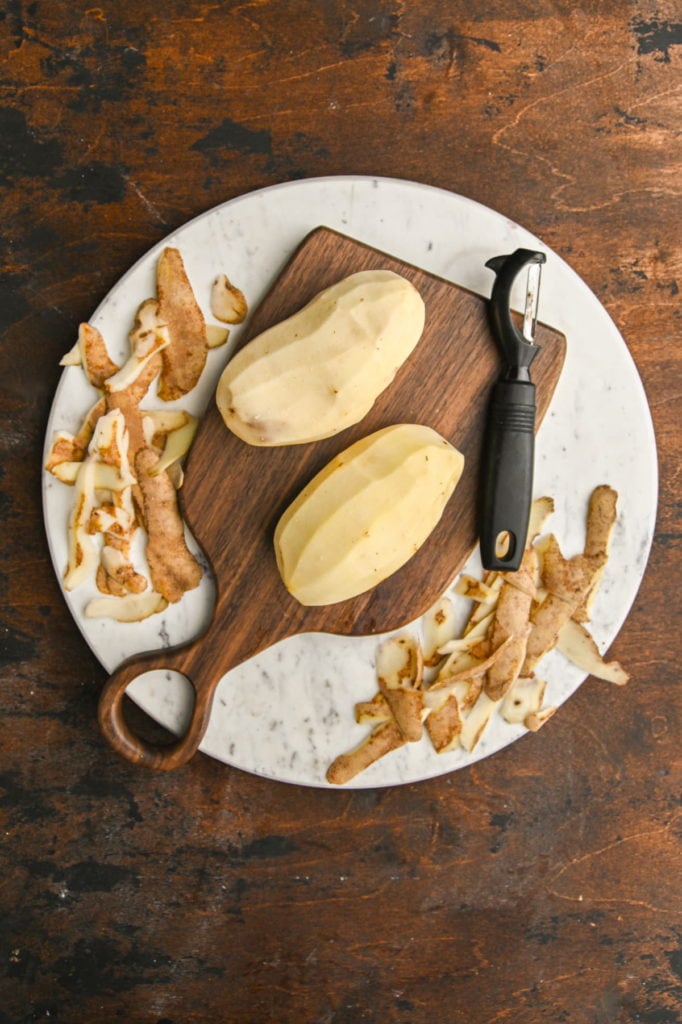 using a vegetable peeler to peel skin off of two russet potatoes