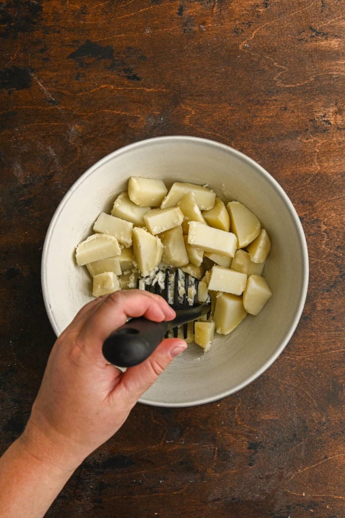 using a potato masher to smash boiled potatoes