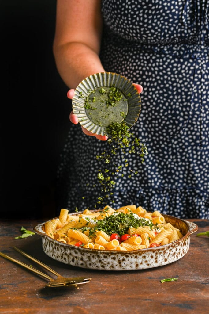 Adding chopped basil to rigatoni.