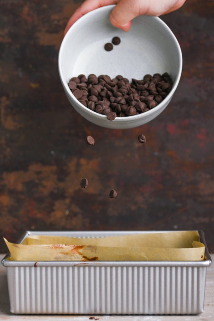 sprinkling chocolate chips on top of condensed milk brownies in baking pan