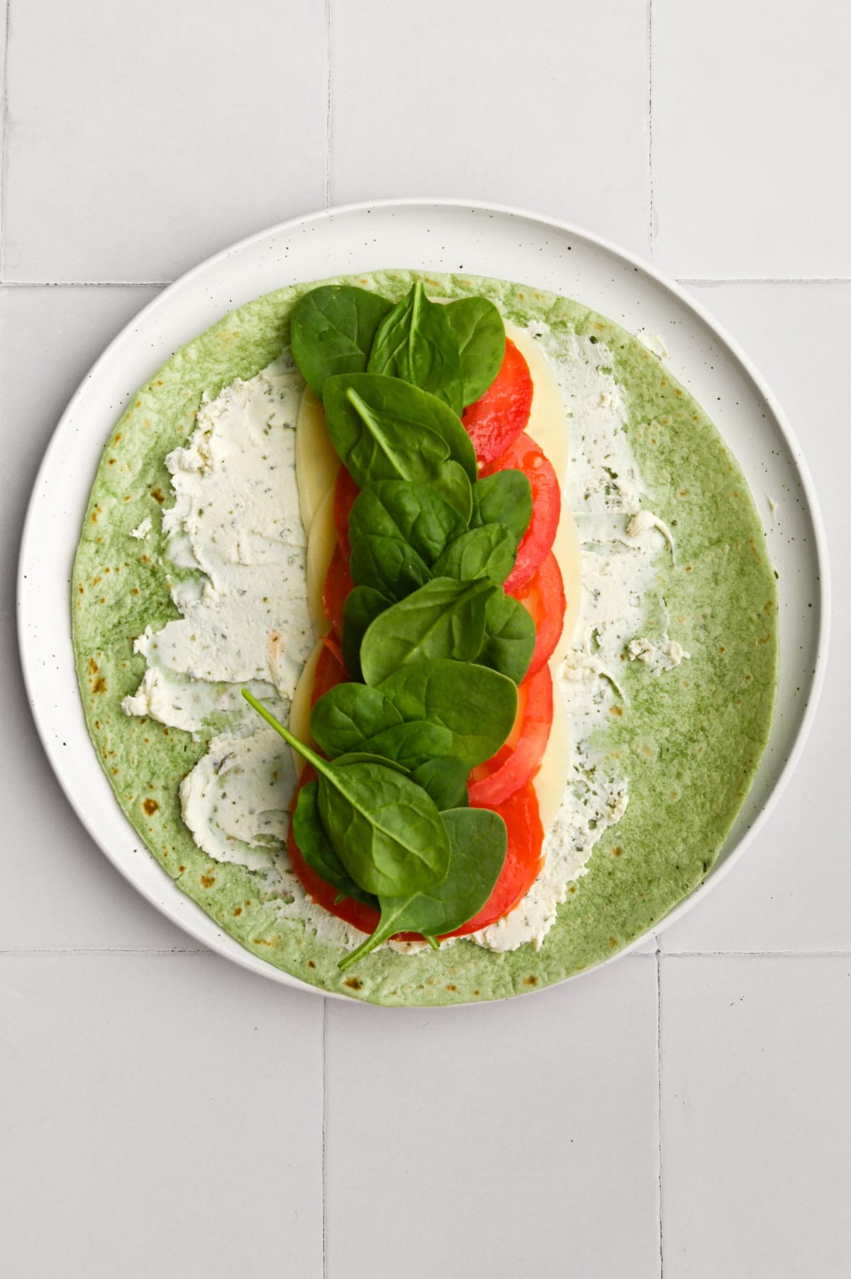 adding spinach to wrap with herbed cheese, provolone, and sliced tomatoes