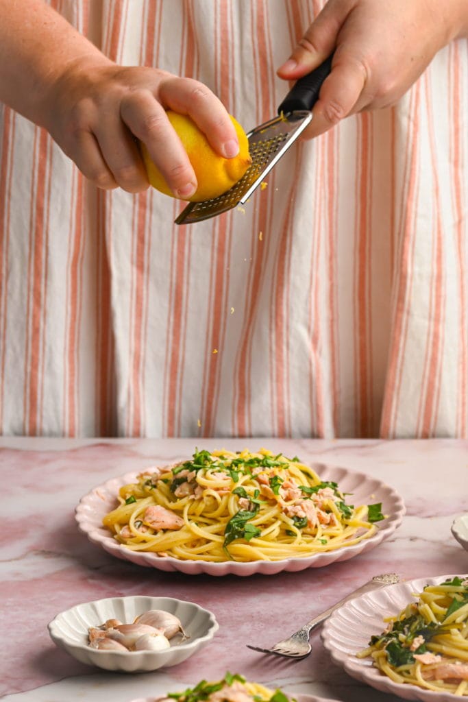 adding extra lemon zest to plated salmon spinach pasta