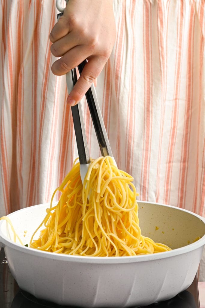 adding cooked pasta to white wine sauce with spinach and salmon