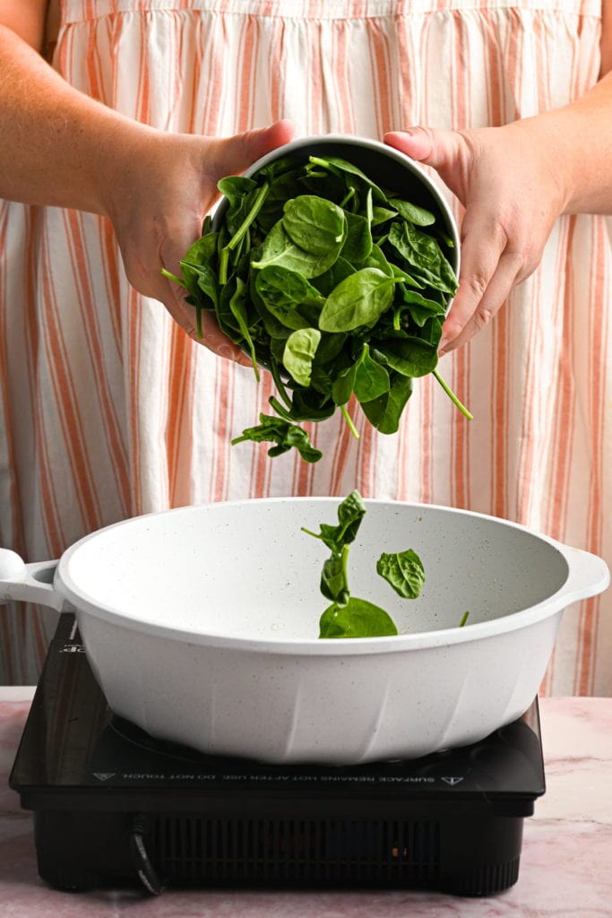 adding spinach to pot with garlic and oil