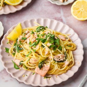 plated salmon spinach pasta with white wine sauce served with a lemon wedge