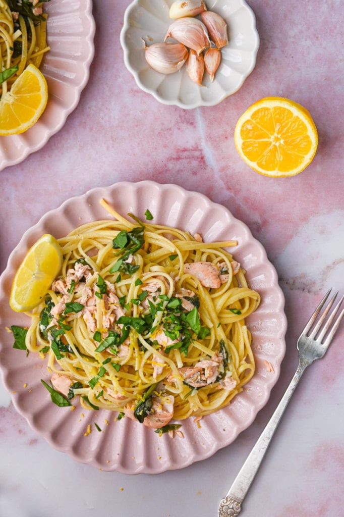 overhead shot of salmon spinach pasta on a pink plate with a lemon wedge