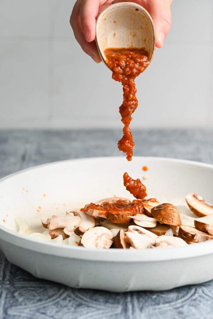 adding salsa to a pan with olive oil, mushrooms, and onions