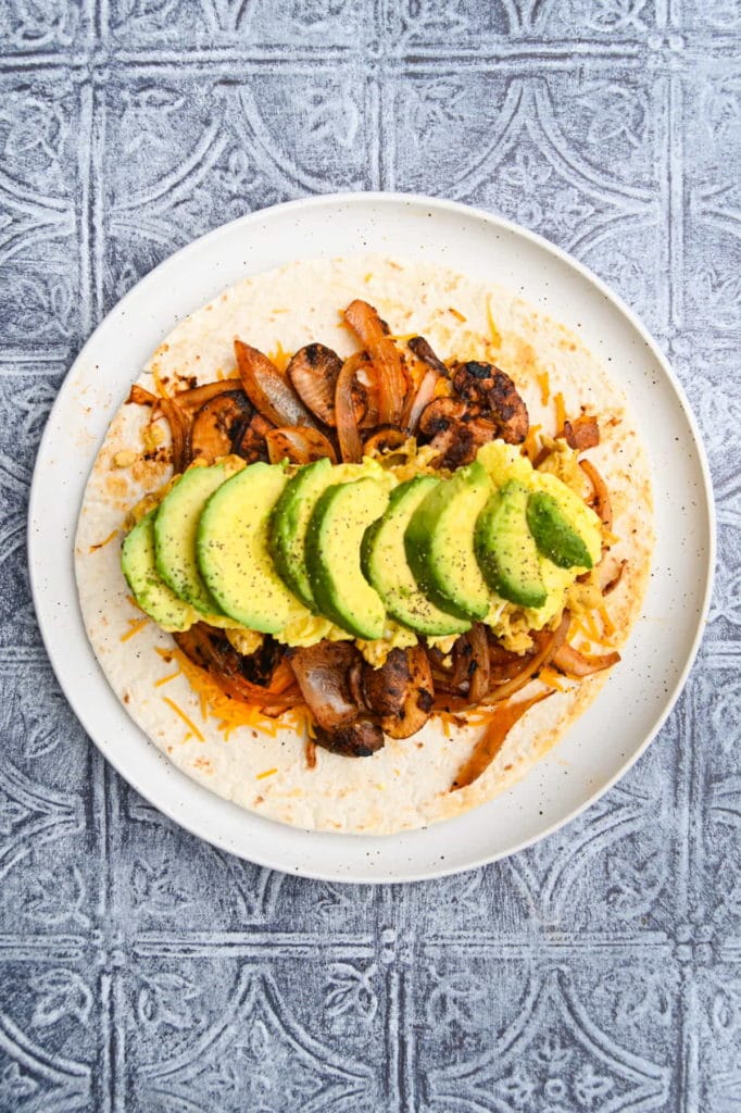 Adding sliced avocado to vegetarian breakfast burrito.