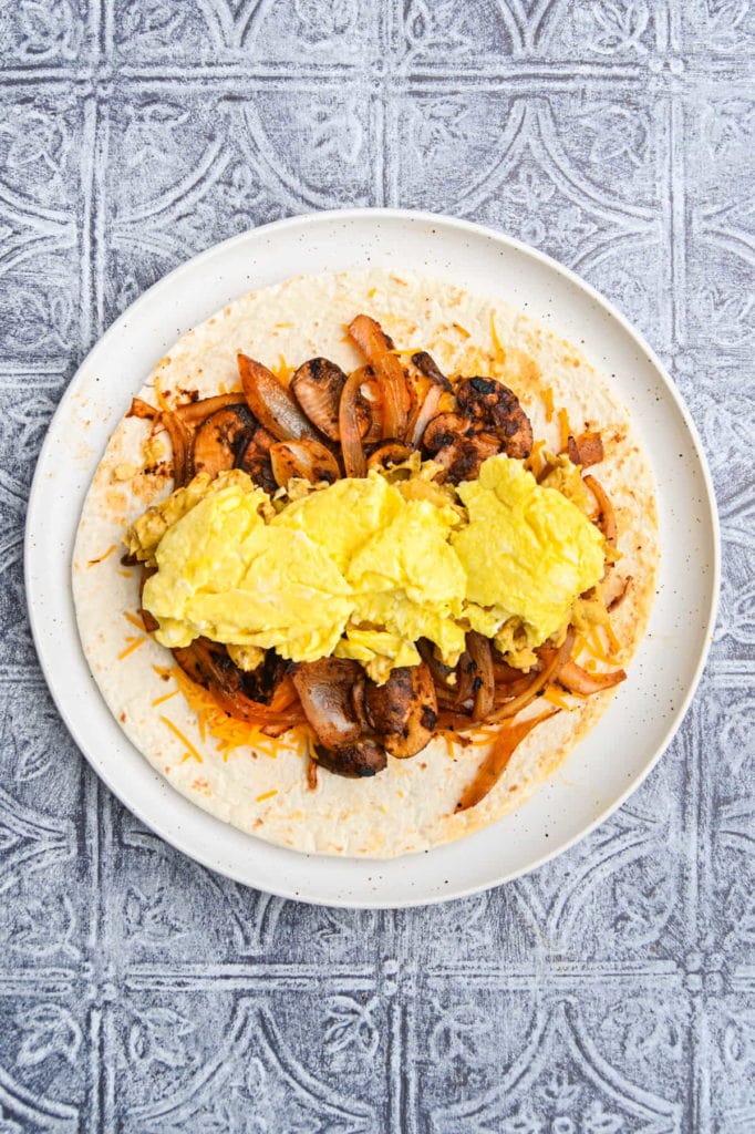 Adding scrambled egg to vegetarian breakfast burrito.