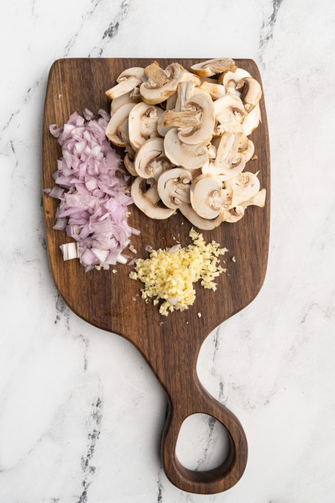 diced scallions, minced garlic, and sliced mushrooms on a cutting board