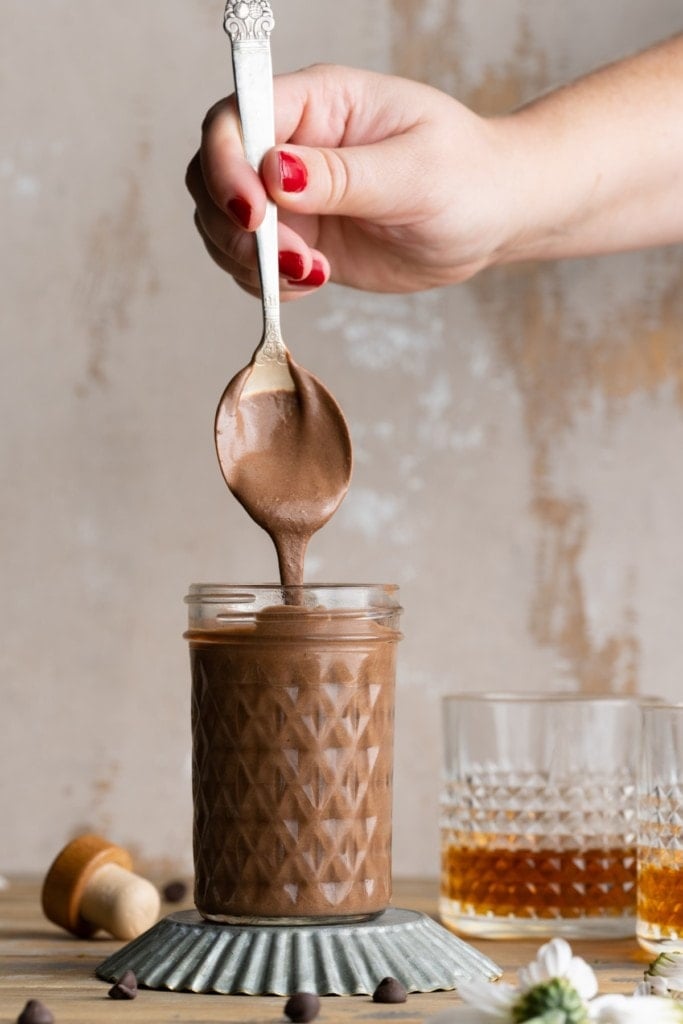 bourbon chocolate sauce in a glass jar with some dripping off a silver spoon