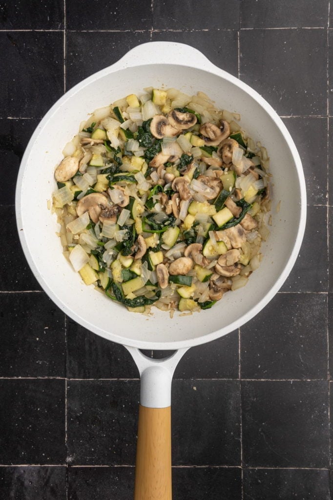 cooking mushrooms, zucchini, onion, garlic, and spinach in olive oil, salt, and pepper