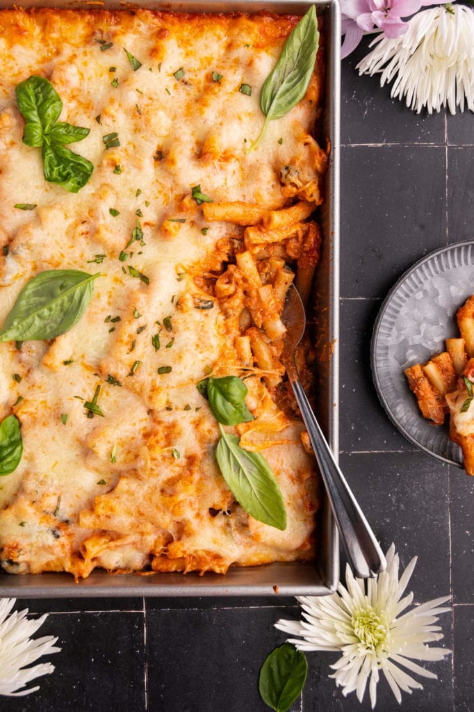 giant casserole dish with baked ziti next to one portion on a plate