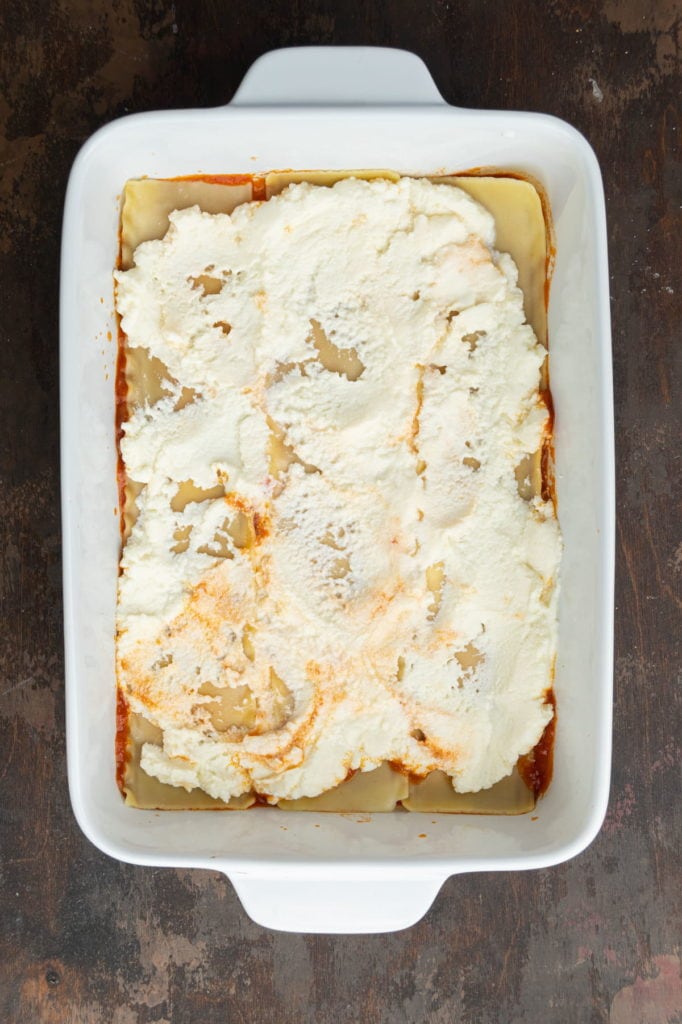 Thin layer of ricotta spread over lasagne noodles in a baking dish.