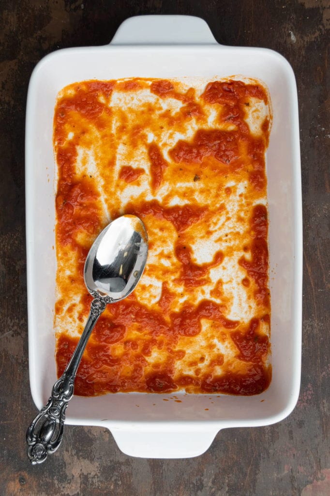 adding layer of marinara sauce to bottom of baking dish