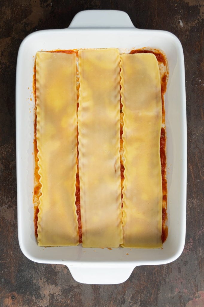 A layer of cooked lasagna noodles on top of marinara.