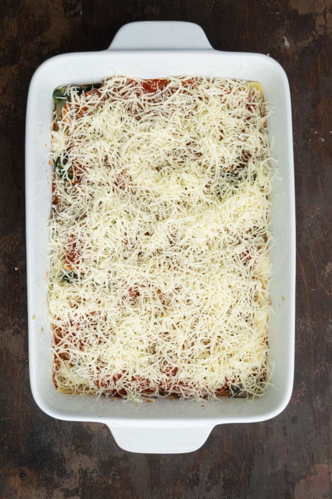 An even layer of shredded cheese on top of vegetables in lasagna.