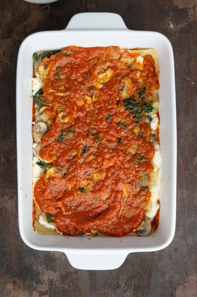 Layer of marinara sauce on top of cooked vegetables in vegetarian lasagna.