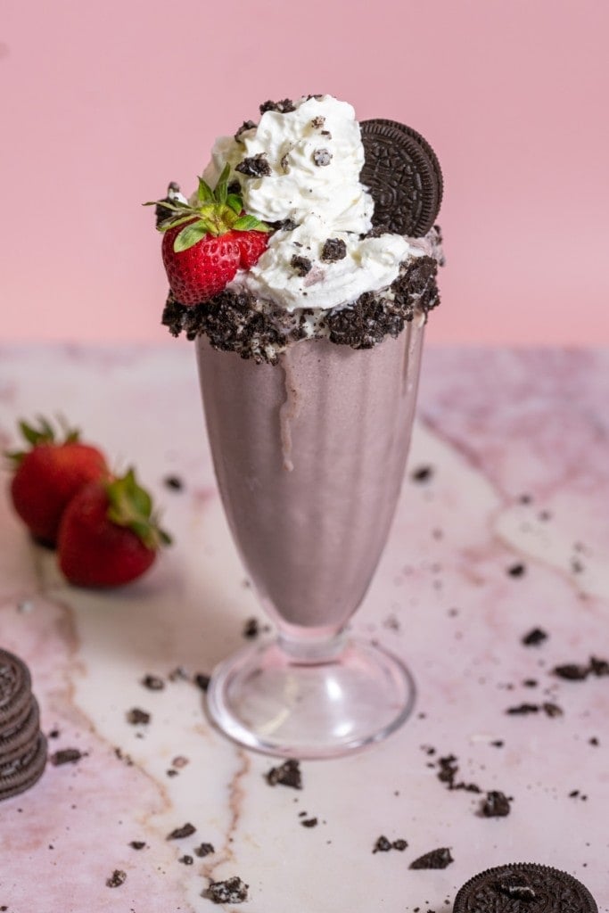 Strawberry Oreo Milkshake garnished with a crushed cookie rim, whipped cream, and a real strabwerry.