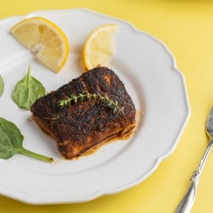 20 minute blackened cod on a plate with two lemon wedges and a couple of pieces of spinach