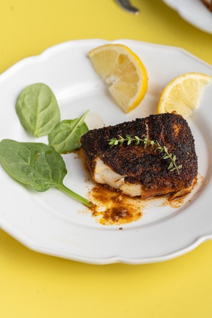 blackened cod with bite taken out of it on a white plate