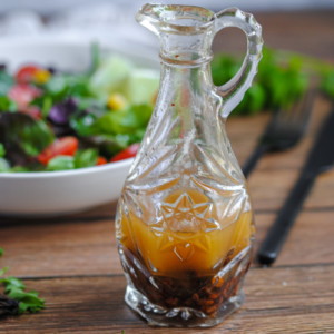 Chipotle Vinaigrette in a small glass cruet on a wooden table with a salad in the background