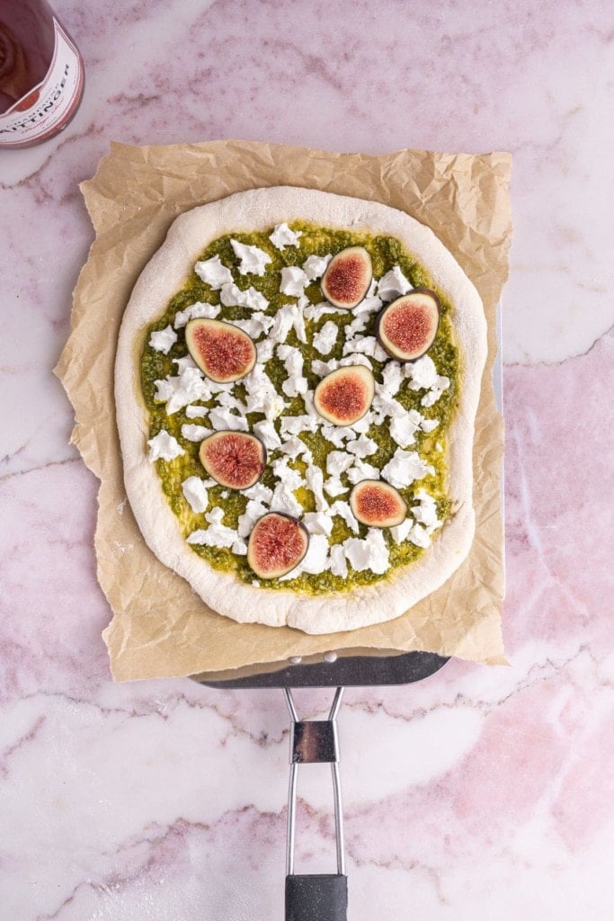 Adding goat cheese and figs overtop of pesto on pizza dough