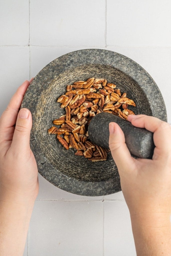 using pestle and mortar to crush pecans