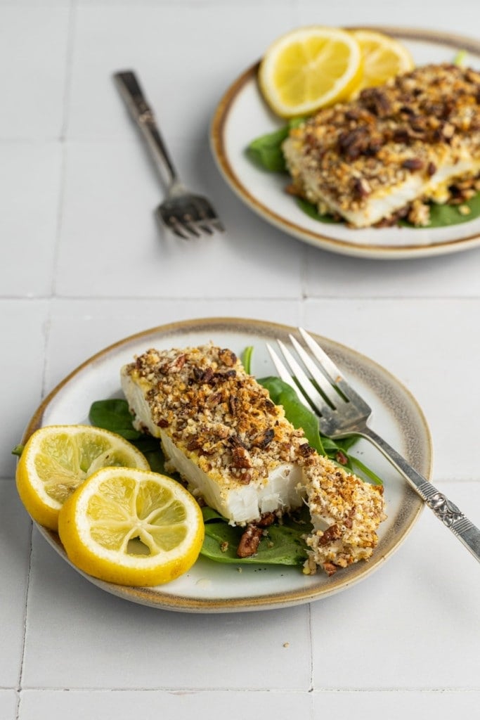 Pecan Crusted Halibut on a plate with lemon wedges sliced open to reveal flaky inside