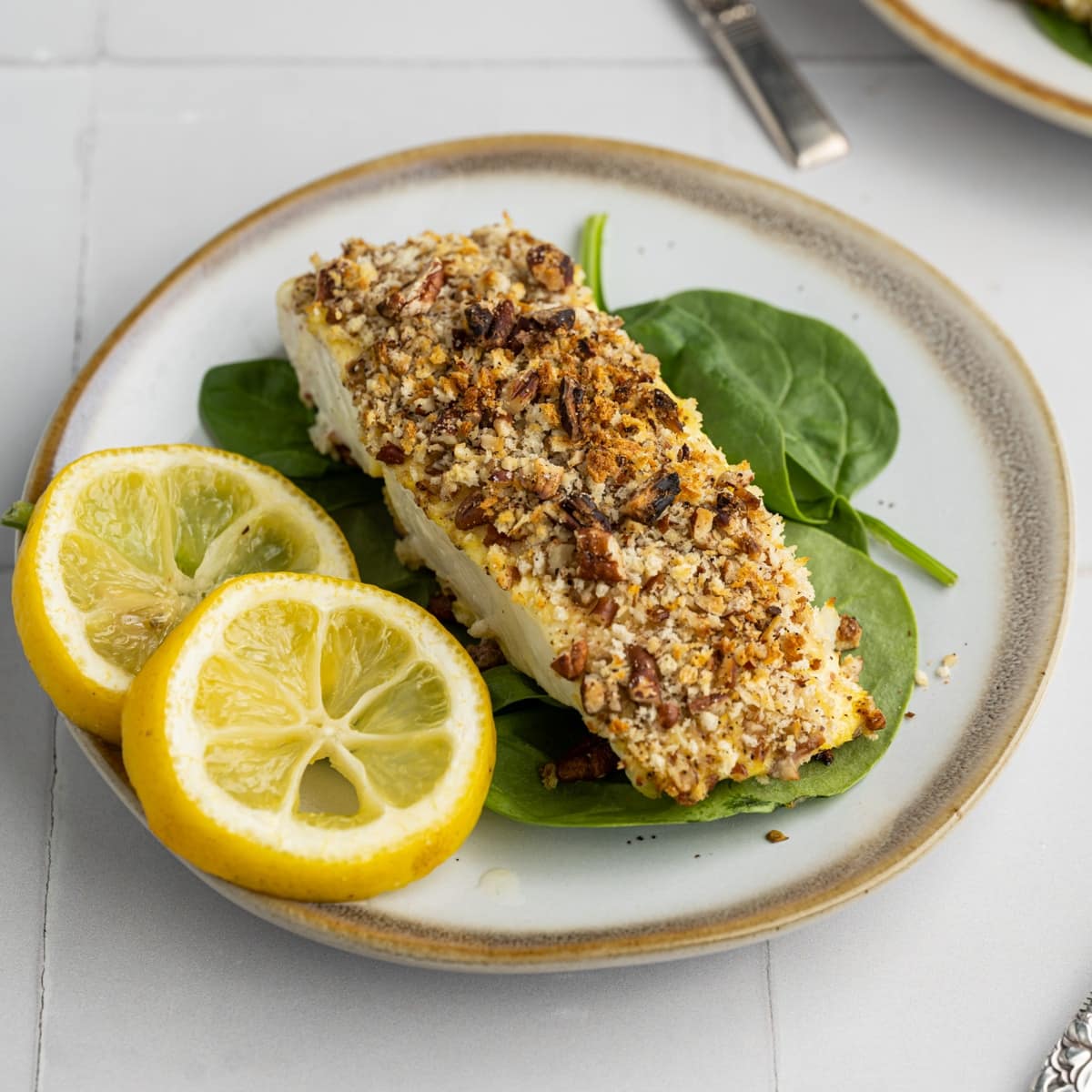 Pecan Crusted Halibut on a plate with spinach and two lemon wedges