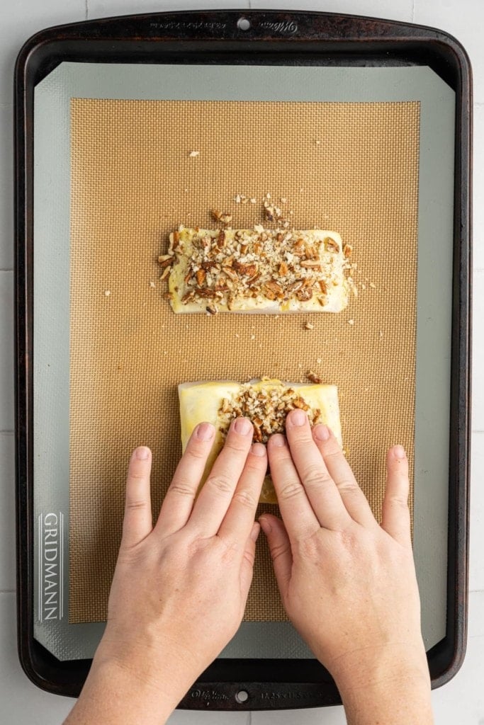 using clean hands to press pecan crust into halibut