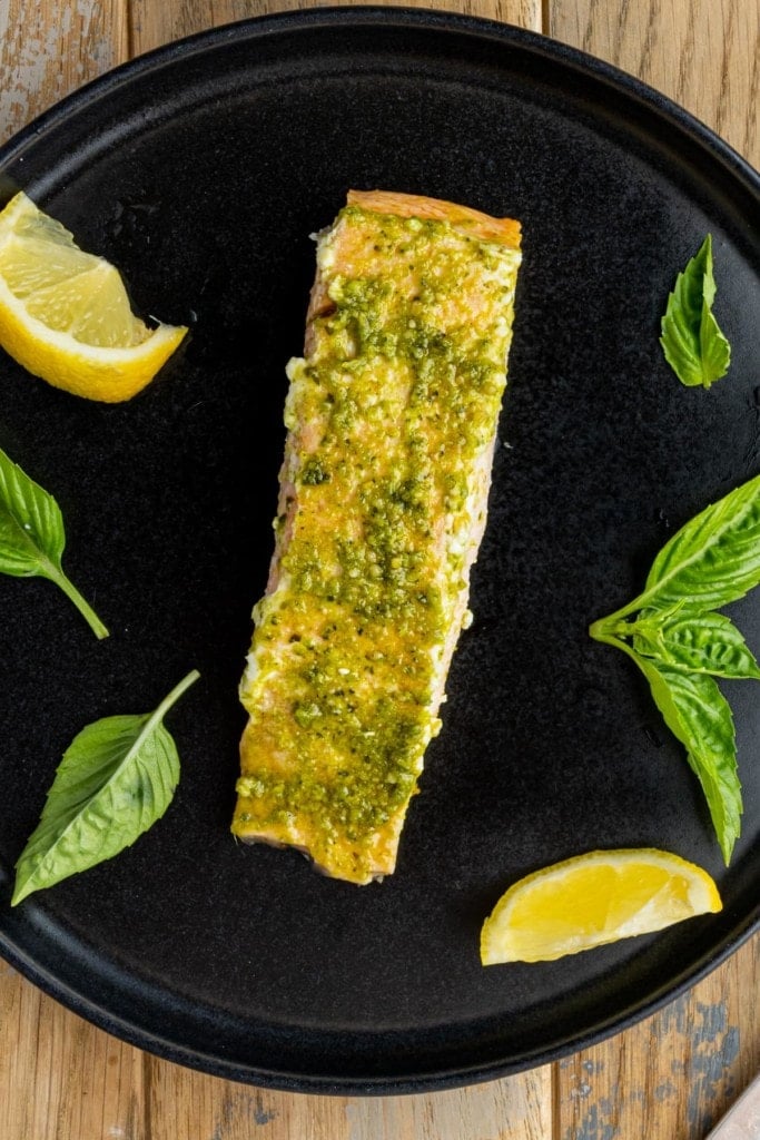 pesto butter salmon plated with basil and lemon wedges