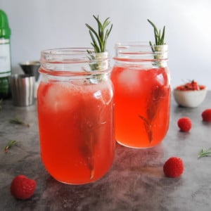 two mason jars with red rosemary foghorn cocktail inside, garnished with a sprig of rosemary
