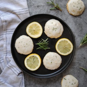 Overhead view of Rosemary Shortbread Cookies with Lemon Glaze on a black plate with decorative slices of lemon