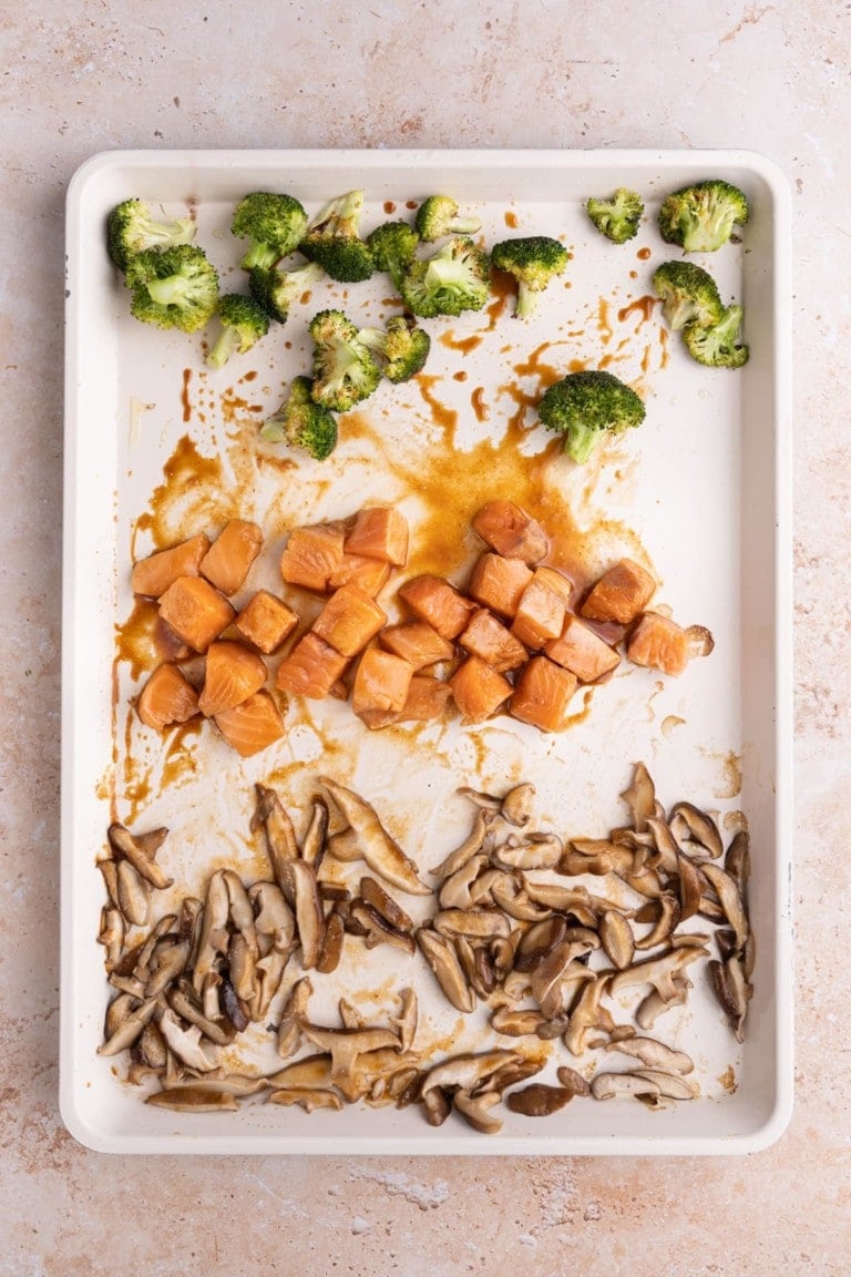 Adding salmon and marinade to baking sheet with the roasted vegetables