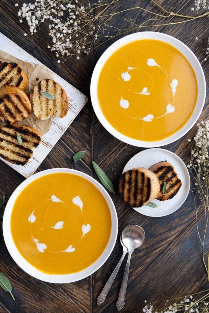 Overhead shot of two bowls of Sweet Potato Soup surrounded by toasted bread