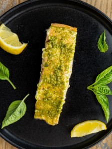 pesto butter salmon plated with basil and lemon wedges