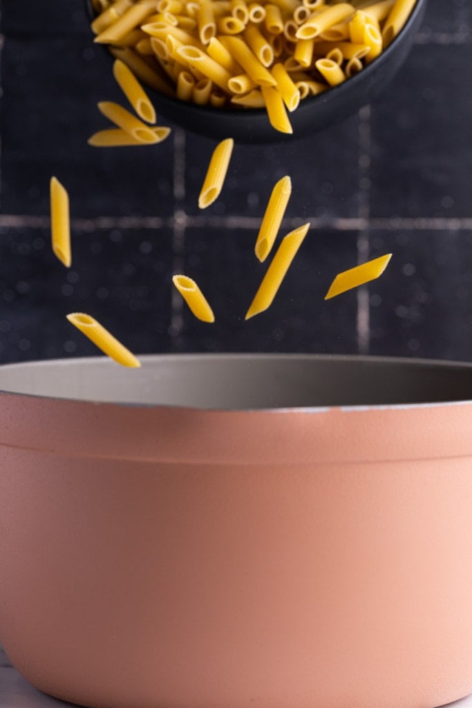 penne pasta falling into a pot of boiling water