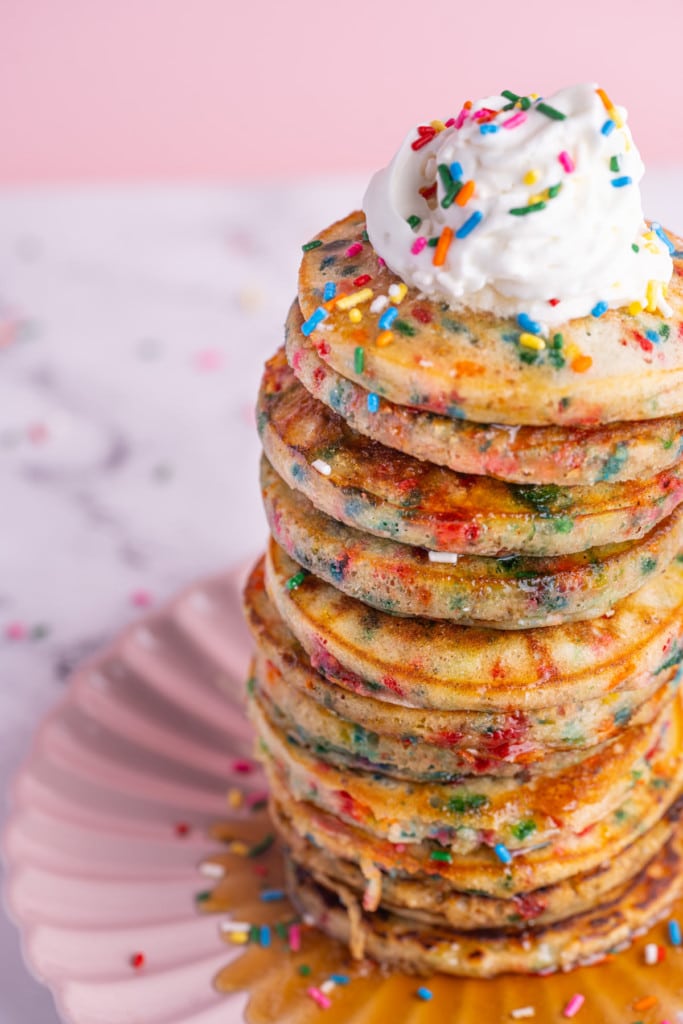 Close up 45 degree angle of tall stack of pancakes with sprinkles and whipped cream on top