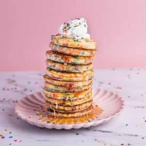 Tall stack of Funfetti Pancakes with whipped cream and syrup