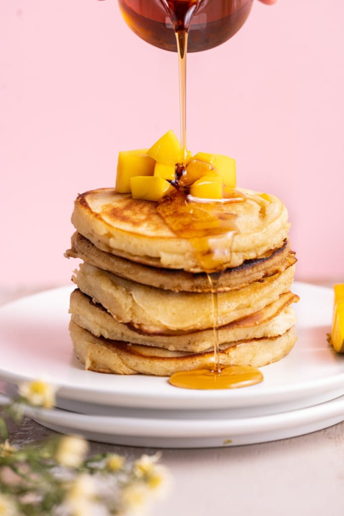 Pouring maple syrup over a stack of 5 mango pancakes