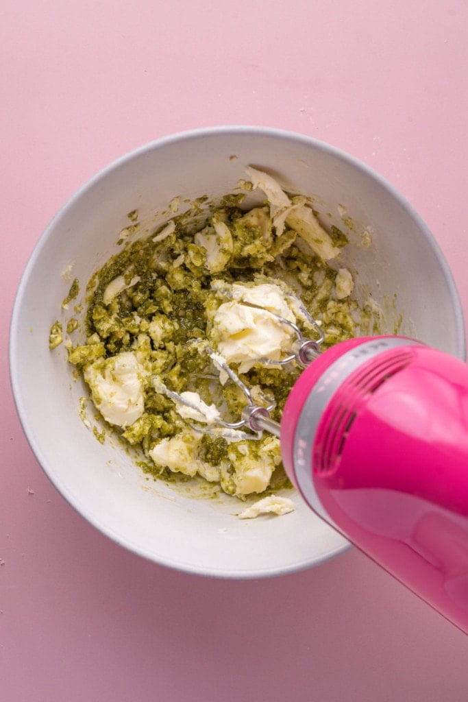 Using a hand mixer to mix pesto and softened butter together