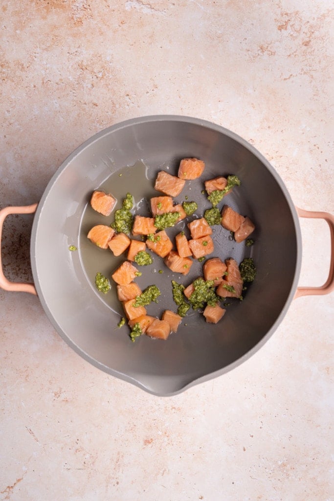 Adding salmon to pot with pesto to cook