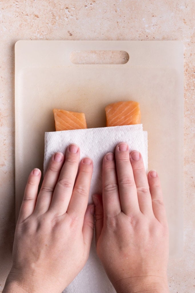 Patting dry salmon with a clean paper towel to reduce moisture