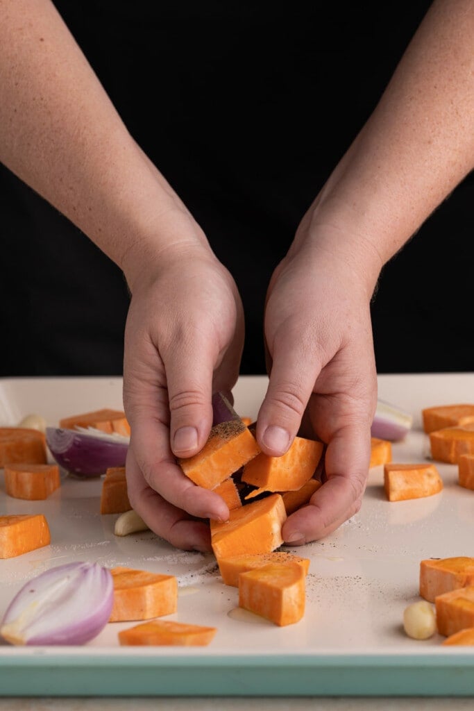 Using clean hands to coat veggies in olive oil, salt, and pepper